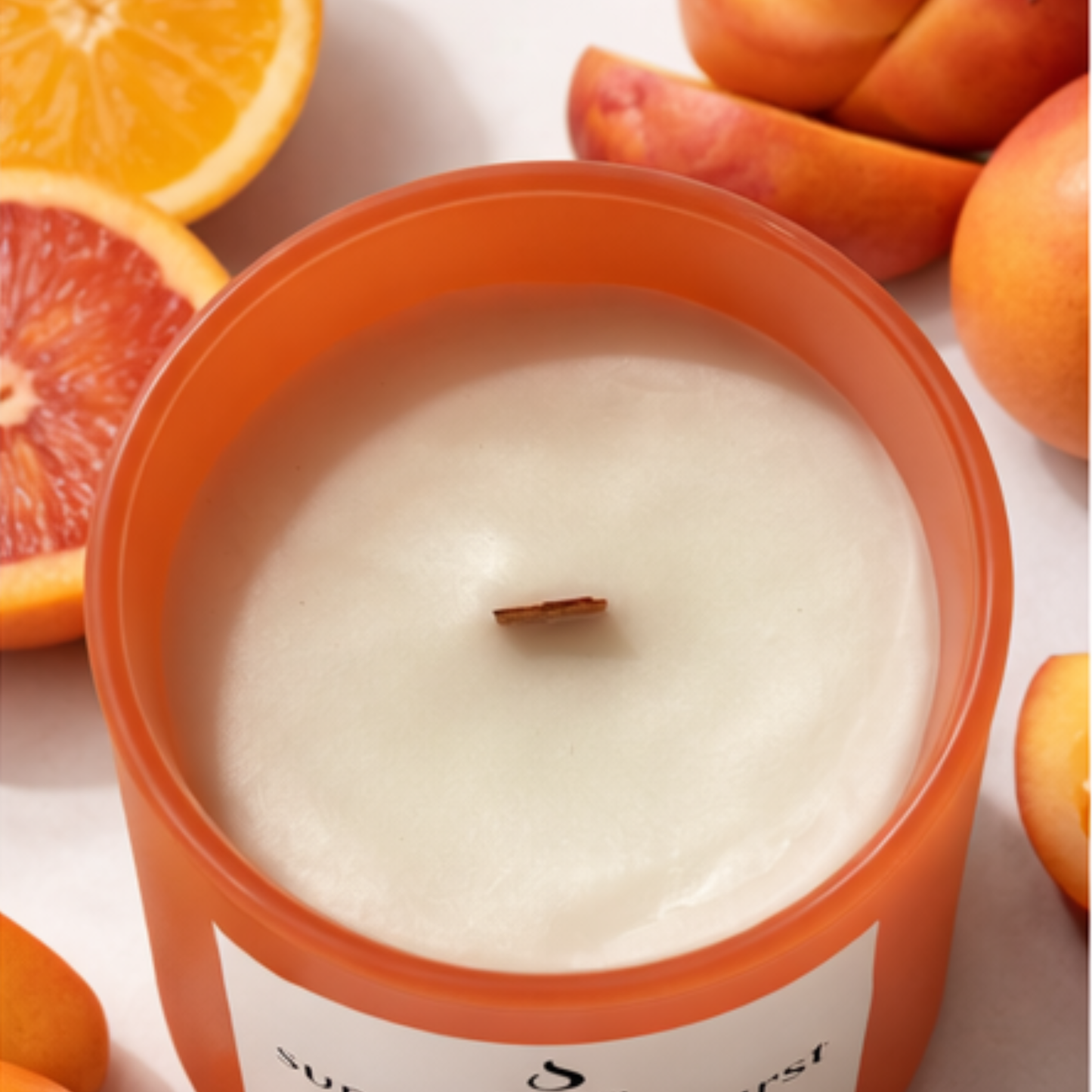 Candle in an orange container surrounded by oranges and apricots on a light background