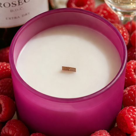 Pink candle with a wooden wick surrounded by raspberries and a bottle of Rosé wine.